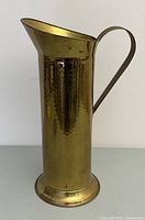 Front view of tall brass finish hammered metal umbrella stand showing flared top and handle.