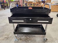 Front view showing top shelf with raised edges, one lockable drawer with handles, and bottom shelf. Diamond plate pattern on front drawer panel.