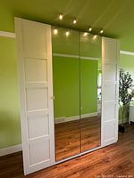 Front view of closed wardrobe showing white shaker-style panels, two central mirrored doors and three top spotlights
