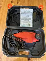 Black & Decker electric hand planer with cord inside black plastic carrying case, instruction manual on top.