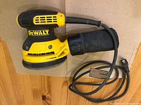 Side view of yellow and black DEWALT random orbit sander with dust collection bag and power cord.