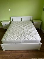 Front view of white full/double bed frame with mattress and two nightstands against green wall