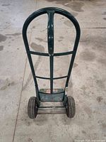 Full front view of green steel P-handle hand truck with two 8 inch solid rubber wheels and loading plate with American flag sticker.