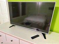 LG 32-inch TV sitting on a dresser with a remote control placed beside it, showing the physical condition and included remote.