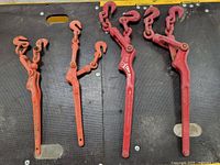 Four red load binders laid on black textured surface, showing 2 large and 2 medium sizes with hooks and ratcheting handles