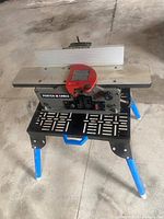 Angled top-side view showing aluminum tables, red cutter guard and folding stand