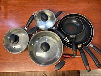 Overview of 3 pots with lids and 4 frying pans in various sizes on wooden surface.