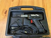 Soldering tool with power cord in molded carrying case with handle, showing top view with soldering tip and trigger