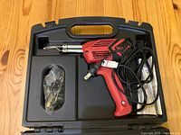 Red and black Weller electric soldering iron with cord, placed inside open black plastic carrying case showing tool and accessories.