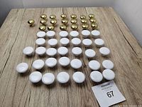 Top view of 32 white porcelain and 19 brass drawer knobs arranged in rows on a wooden surface.