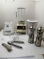 View of all kitchen items including two blenders, two pepper grinders, garlic press, measuring cup and can opener.
