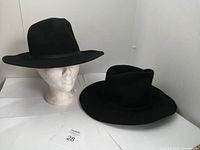 Two black cowboy hats displayed on white mannequin heads and flat surface, showing brim shapes and style.