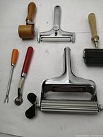 Photo showing six vintage kitchen tools including rollers, cutters, fish skinner, and cheese slicer.