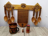 Full lot including wall decoration with spoons, cutting board, mug and two Matryoshka dolls displayed on a wood surface against a white background.