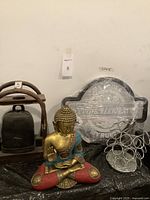 Full lot shot showing all items: Buddha statue in front, wooden framed bell on left, glass car-themed sign in back, and chrome pod carousel on right