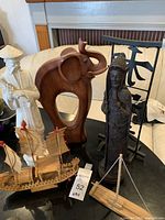 Photo showing white ceramic statue, wooden elephant, black Asian figure statue, black metal signage, and wooden ship model.