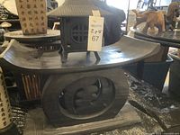 Wooden stool with carved Asian character cutouts and smooth curved top sitting beneath a metal lantern with pagoda roof design.