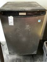 Front view of Danby small refrigerator showing brushed aluminum door and black plastic top trim, with some surface wear and dust.