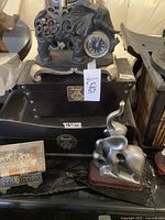 Photo of silver-tone elephant clock statue on top of a dark wooden jewelry box, silver-tone resin elephant on wooden base in front, and a decorative silver-tone embossed box on left side.