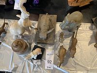 Overview of eight statues of elephants and other animals made of ceramic, metal, and stone on a covered table surface.