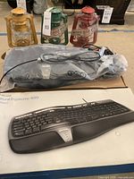 Photo showing three metal wick lanterns in yellow, green, and red colors placed behind a new Microsoft Natural Ergonomic 4000 keyboard in packaging, with original box.