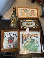 Wide view of all five displayed framed bar art pieces. Includes Corner Bar Friendly Service bottle-shaped sign, Kaiserdom Pilsener framed print, Midori Melon Liqueur framed poster, Wet & Wild cocktail recipe framed print, and Private Bar framed mirror sign.