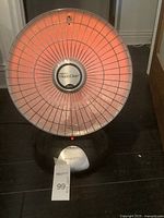 Front view of the Presto HeatDish heater showing the heating element glowing orange inside the wire guard above the black base.