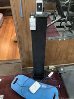 Full view of Craig black speaker tower with iPhone dock, showing iPhone docked on top, exercise board on floor, USB outlet visible.