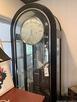 Full view of the black wooden and glass grandfather clock showing its height and structure.
