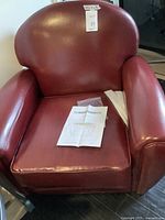 Front view of red faux leather club chair with instruction papers on seat cushion