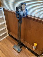Full view of Shark Rocket upright vacuum cleaner against wall, showing handle and upright position with blue and gray color.