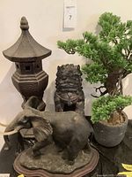 Photo showing resin Fu dog statue, resin elephant statue, ceramic pagoda statue, and plastic bonsai tree grouped together