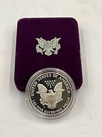 Photo showing the 1986 American silver dollar coin in protective case resting on top of the purple velvet box with a silver eagle emblem.