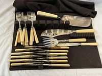 27-piece 19th century cutlery and serving set by Walker & Hall with cream-colored handles on black display mat, including fish serving utensils and forks.