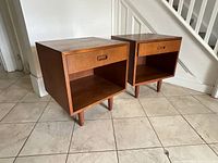 Pair of tables angled front view showing drawer fronts, open shelves and legs