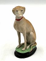 Front-angle view of the antique bisque porcelain greyhound whippet dog figurine sitting on green and black base