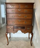 Front view of entire highboy chest showing eight drawers, hardware, cabriole legs and scalloped skirt.