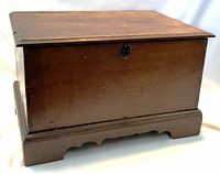 Front and angle view of antique dowry chest showing dark wood, flat lid, dovetail construction, and inlaid initials.
