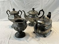 Front angled view of four antique pewter tea service pieces on white cloth background