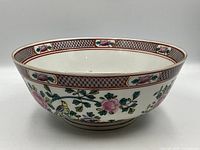 Front and side view of the bowl showing hand-painted pink roses, green leaves, and yellow bird motifs on white porcelain with decorative geometric border.