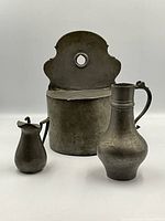 Photo showing all three antique pewter items together including candle box, small vase, and lidded pitcher.
