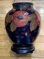 Front view of vase showing large pomegranate fruits and seed clusters on rich blue ground, on wooden stand