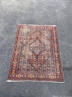 Full view of the rectangular hand woven area rug laid flat on an outdoor paved surface, showing the overall design, color, and condition.