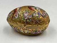 Closed egg-shaped box showing gilt background with enameled birds and floral motifs