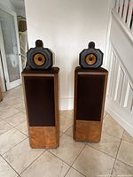 Pair of speakers with cloth grilles removed showing top midrange/tweeter modules and burl veneer cabinets.