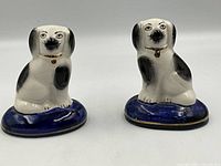 Front view of both vintage Staffordshire spaniel dog figurines showing seated pose on blue bases with gold trim.