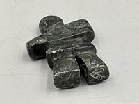 Photo showing top and slightly angled view of the dark soapstone Inukshuk sculpture lying down, showing surface texture and white veining with artist's signature on one foot.