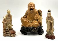 Three soapstone figurines on wood stands arranged side by side against white background