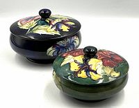 Two lidded jars side by side on white background, small green jar in front, large blue jar behind