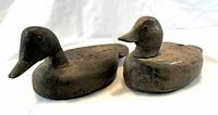 Two antique pine duck decoys viewed from front angle on white fabric background.